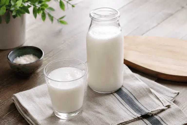 Glas melkkefir en fles karnemelk op een houten tafel met kefirkorrels op de achtergrond, ter illustratie van het verschil tussen melkkefir en karnemelk.